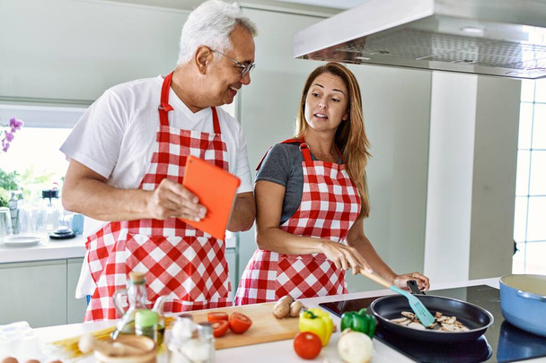 Középkorú spanyol pár mosolyog boldog főzés és használata touchpad a konyhában. - Fotó, kép