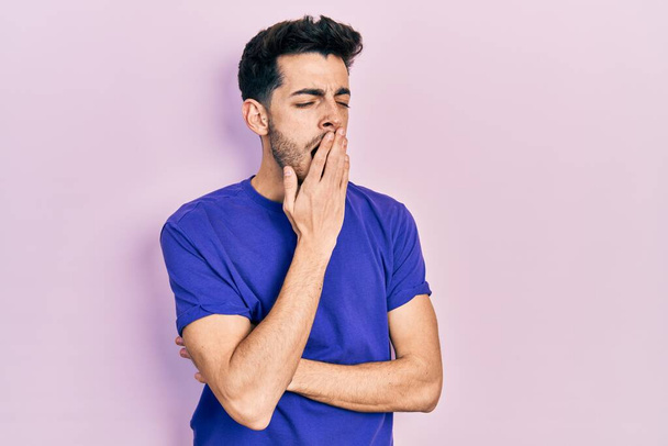 Jeune homme hispanique portant t-shirt décontracté ennuyé bâillement fatigué couvrant la bouche avec la main. agitation et somnolence.  - Photo, image