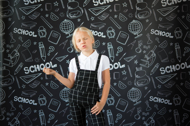 цікава маленька дівчинка в шкільному одязі проти шкільної дошки з малюнками на тему школи. Шкільна концепція. Назад до школи
. - Фото, зображення