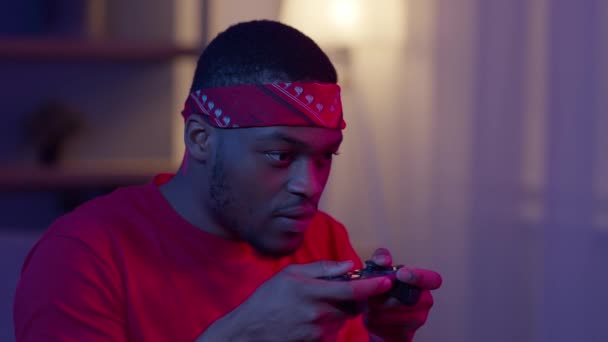 アフリカ系アメリカ人ゲーマーの男が自宅で座ってビデオゲームをプレイ - 映像、動画