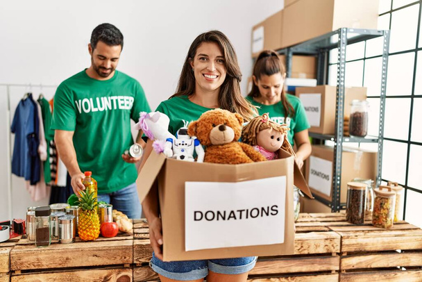Grupa hiszpańskich wolontariuszy pracujących w ośrodku charytatywnym. Kobieta uśmiechnięta szczęśliwy holding box z zabawkami do oddania. - Zdjęcie, obraz
