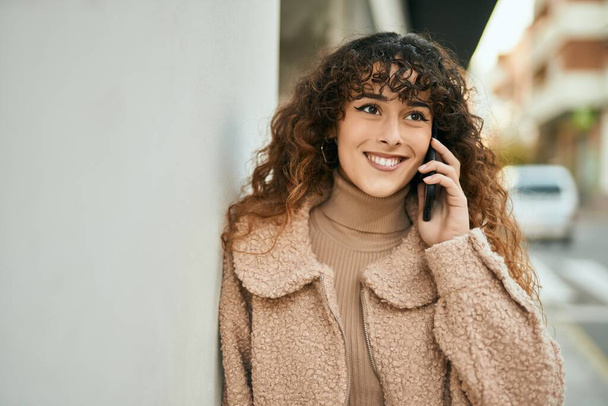 Νεαρή Ισπανίδα γυναίκα χαμογελά ευτυχισμένη μιλώντας στο smartphone της πόλης - Φωτογραφία, εικόνα