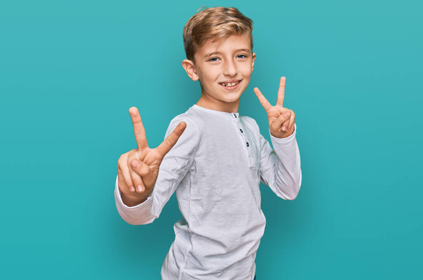 Petit garçon caucasien portant des vêtements décontractés souriant en regardant la caméra montrant des doigts faisant signe de victoire. numéro deux.  - Photo, image