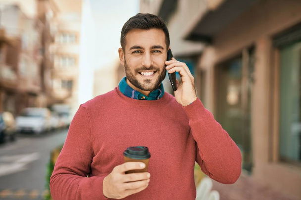 Joven hispano hablando en el smartphone tomando café en la ciudad. - Foto, imagen