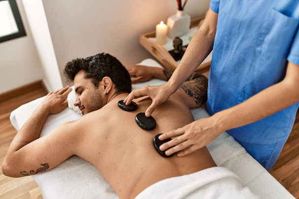 Man ontvangt rug massage met zwarte stenen bij beauty center. - Foto, afbeelding