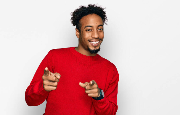 Fiatal afro-amerikai férfi szakállal, alkalmi téli pulóvert visel, ujjal mutogat a kamerára, boldog és vicces arccal. jó energia és rezgések.  - Fotó, kép