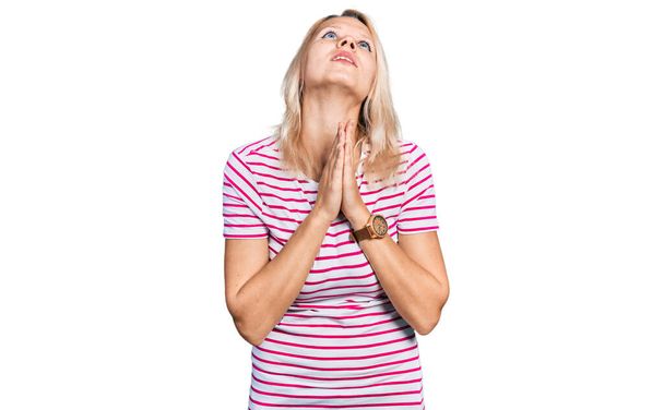 Jonge blanke vrouw draagt casual kleding bedelend en biddend met handen samen met hoop uitdrukking op gezicht zeer emotioneel en bezorgd. bedelen.  - Foto, afbeelding