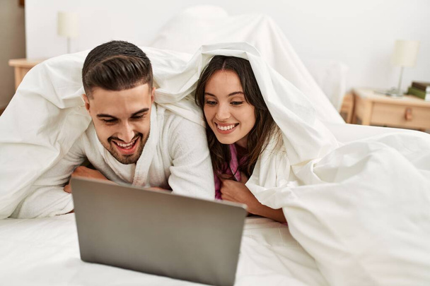 Young hispanic couple watching movie using laptop lying in bed. - Fotoğraf, Görsel