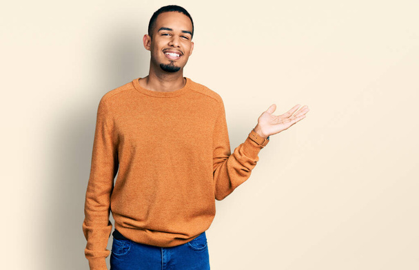 Giovane uomo afroamericano indossa abiti casual sorridente allegro presentazione e puntando con il palmo della mano guardando la fotocamera.  - Foto, immagini