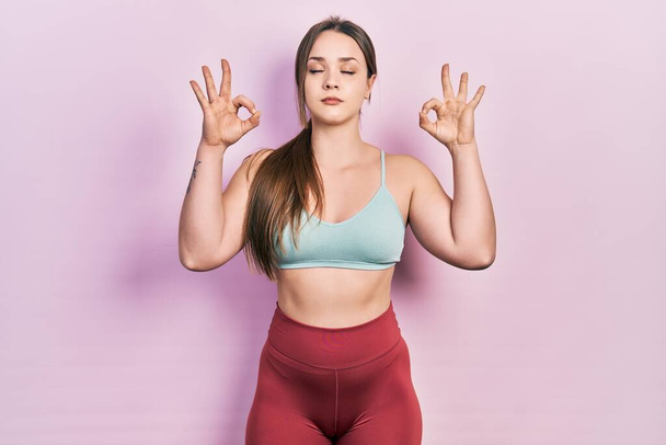 Young hispanic girl wearing sportswear relax and smiling with eyes closed doing meditation gesture with fingers. yoga concept.  - Foto, afbeelding
