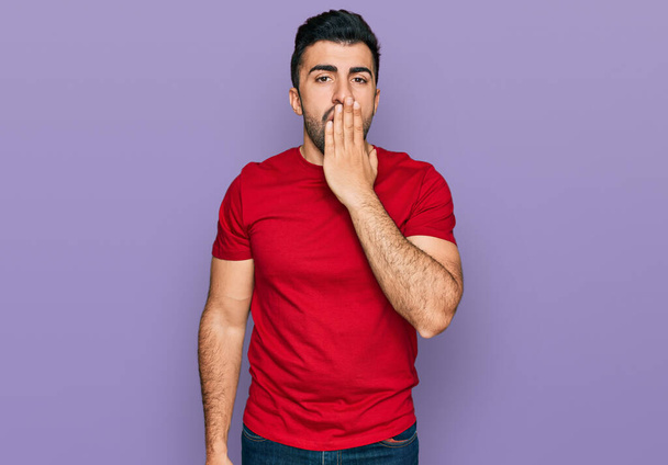 Hombre hispano con barba vistiendo casual camiseta roja aburrido bostezando cansado cubriendo la boca con la mano. inquietud y somnolencia.  - Foto, Imagen
