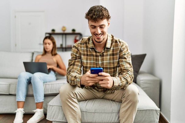 Young hispanic couple smiling happy using laptop and smartphone sitting on the sofa at home. - Fotó, kép