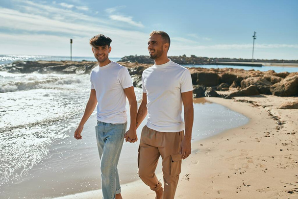 Молодая пара геев улыбается счастливая прогулка по пляжу. - Фото, изображение