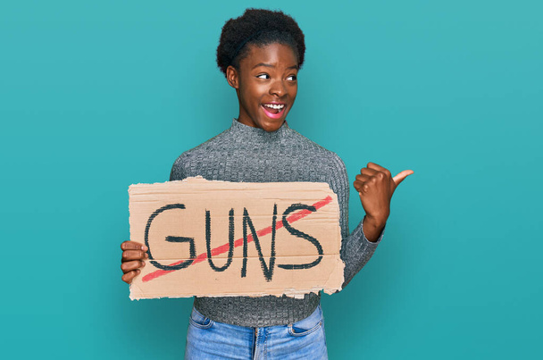 Молодая африканская американка, не держащая в руках оружия предупреждающее знамя указывающее пальцем вверх в сторону улыбается счастливая с открытым ртом  - Фото, изображение