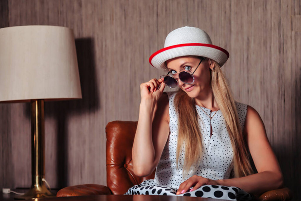 Portrait adult woman actress posing in retro styling clothes with sunglasses in vintage living room. Female in pin-up style black and white dress in polka dot and hat. Concept retro fashion and trend - Fotoğraf, Görsel