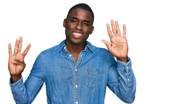 Молодий афроамериканець, одягнений у повсякденний одяг, показує і вказує вгору з пальцями номер дев'ять, посміхаючись впевнено і щасливо.  - Фото, зображення