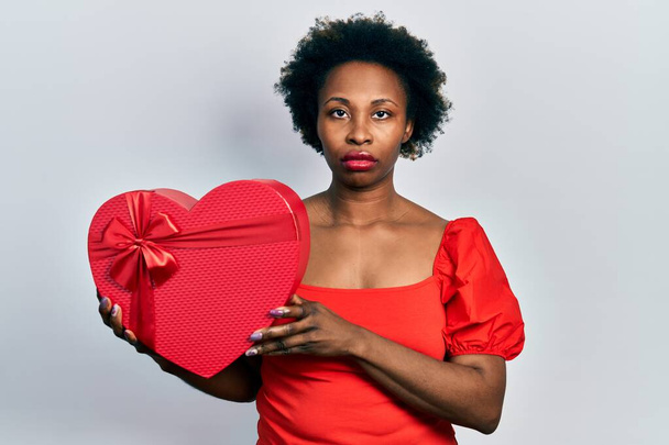 Молодая африканская американка держит валентинку подарок мышления отношение и трезвое выражение лица выглядит уверенным в себе  - Фото, изображение