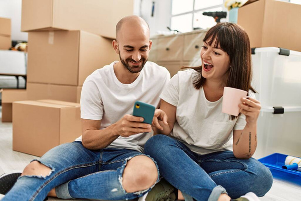 Молода пара іспаномовних посміхається щасливим використанням смартфона в новому будинку
. - Фото, зображення