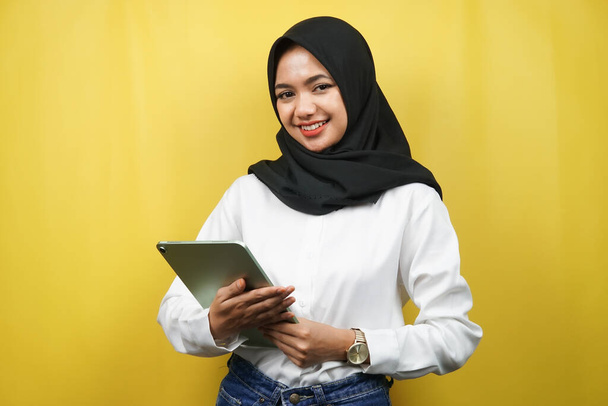 Beautiful young asian muslim woman smiling, excited and cheerful holding tablet, isolated on yellow background - Photo, Image