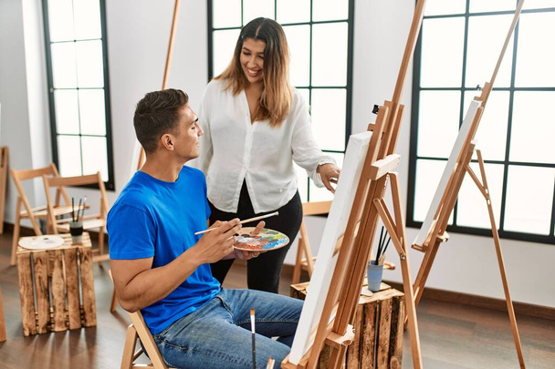 Student and teacher smiling happy painting at art school. - Fotó, kép
