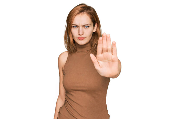 Молодая белая женщина в повседневной одежде перестает петь ладонью. предупреждающее выражение с негативным и серьезным жестом на лице.  - Фото, изображение