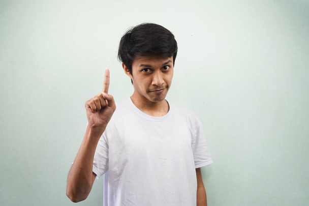 Jonge aziatische man draagt witte t-shirt krijgt een idee, hand wijzen op lege ruimte geïsoleerd op grijze achtergrond - Foto, afbeelding