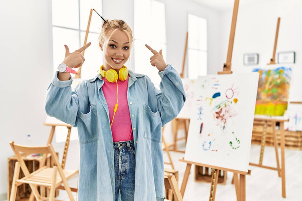 Young caucasian girl at art studio smiling pointing to head with both hands finger, great idea or thought, good memory  - Photo, Image