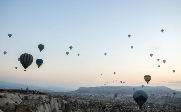 Colorful hot air balloons flying over rock and valley landscape in morning fog at sunrise in Cappadocia, Anatolia, Turkey - Photo, Image