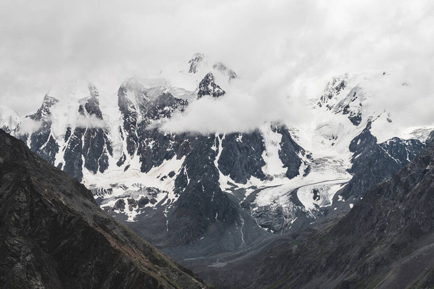 Atmospheric alpine landscape with massive hanging glacier on giant mountain. Big glacier tongue on mountainside. Low clouds among snowbound mountains. Cracks on ice. Majestic scenery on high altitude. - Fotó, kép