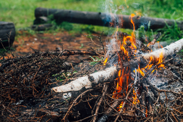 Burning branches and brushwood in fire close-up. Atmospheric warm background with orange flame of campfire and blue smoke. Beautiful full frame image of bonfire. Firewood burns in vivid flames. - Foto, Imagen