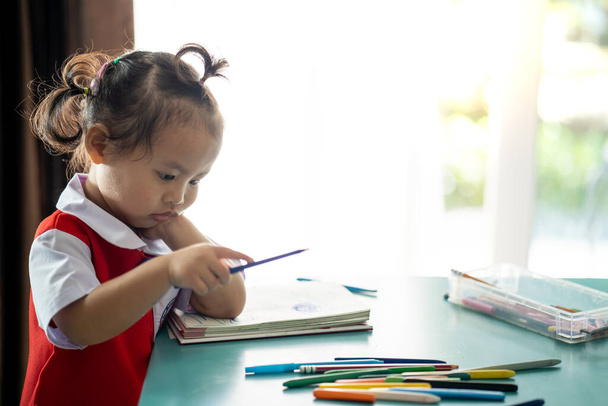 A closeup shot of a Southeast Asian baby girl drawing with colorful pens - Fotó, kép