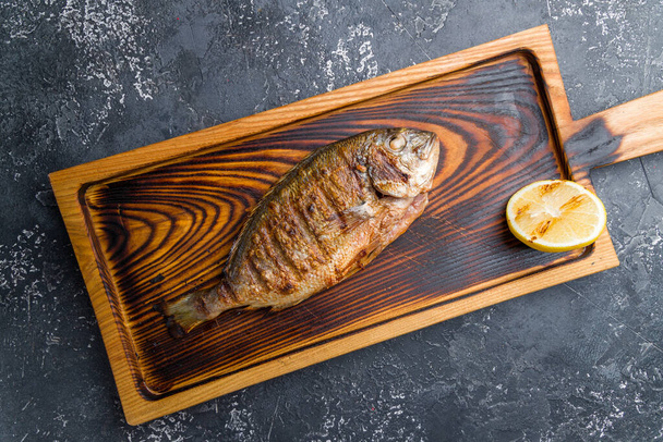 Dorado on grill on beautiful wooden board on black stone table top view - Фото, изображение