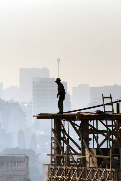 A silhouette of a construction worker on a half-built building - Zdjęcie, obraz