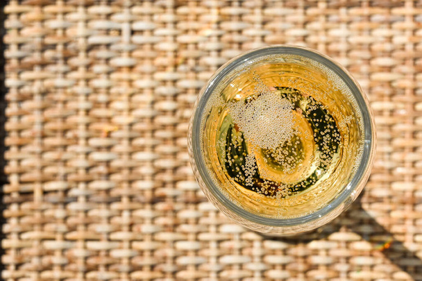 Vista de cerca mirando hacia abajo en una copa de champán en una mesa de jardín de mimbre en una noche de verano. - Foto, imagen