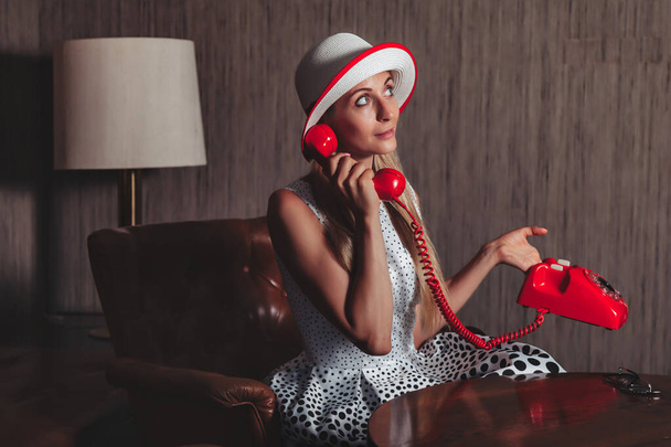 Portrait emotion adult woman actress with old red telephone posing dressed retro styling clothes in vintage living room. Female in pin-up fashion style black and white dress in polka dot and hat - Foto, immagini