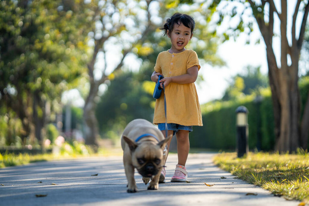 A little Southeast-Asian girl walking her bulldog in a park - Foto, Bild