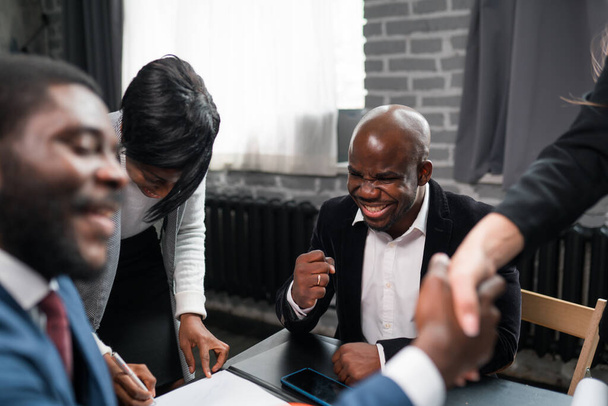 Happy african american businessman rejoices at successful deal while sitting in negotiations with colleagues - Fotoğraf, Görsel