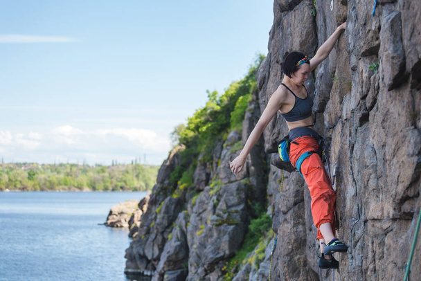 Tyttö on vuorikiipeilemässä veden äärellä. kalliokiipeilijä voittaa vaikean reitin. urheilu ja kunto luonnossa - Valokuva, kuva