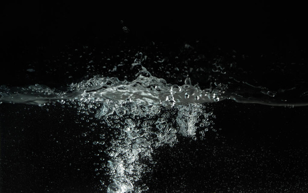 Water splashing as it's poured into aquarium tank, black background - Фото, зображення