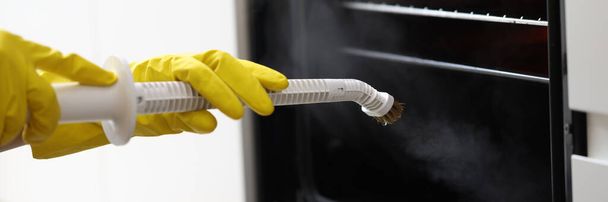 Man in yellow gloves washing oven with steam mop closeup - Фото, изображение