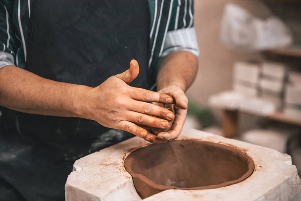 A closeup of an adul man making a clay pot on a table in a workshop - Fotó, kép