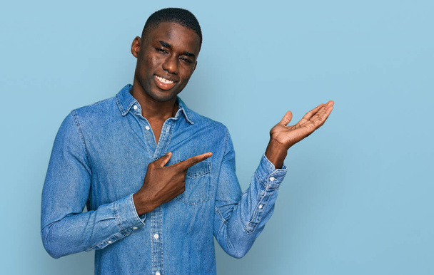 Young african american man wearing casual clothes amazed and smiling to the camera while presenting with hand and pointing with finger.  - Fotografie, Obrázek