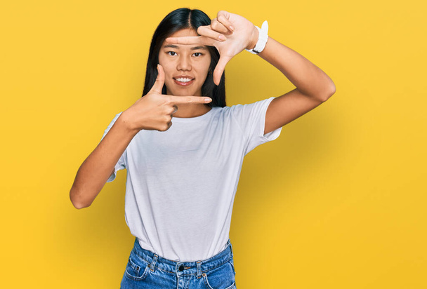 Gyönyörű fiatal ázsiai nő visel alkalmi fehér póló mosolygós így keret kezek és ujjak boldog arcát. kreativitás és fényképezés koncepció.  - Fotó, kép