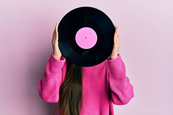 Žena drží retro vinylový disk zakrývající tvář přes růžové pozadí - Fotografie, Obrázek