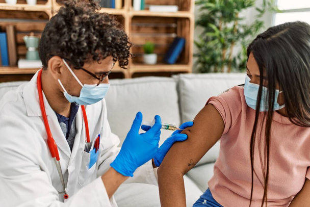 Joven doctor hombre inyectándose la vacuna contra el coronavirus covid-19 para una mujer sentada en el sofá de la clínica. - Foto, imagen