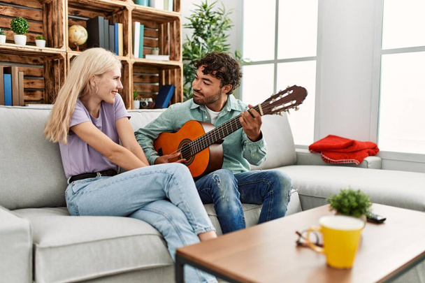 Mies soittaa espanjalaista kitaraa hänen tyttöystävänsä istuu sohvalla kotona - Valokuva, kuva