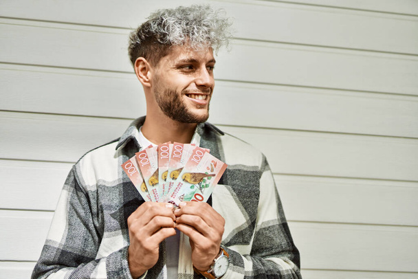 Mladý hispánec se šťastně usmívá a drží ve městě novozélandské dolary. - Fotografie, Obrázek