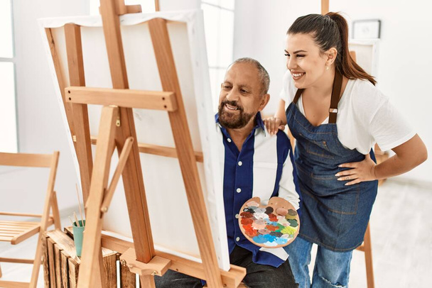 Young painting teacher woman teaching art to senior man painting on canvas at art studio - Foto, imagen