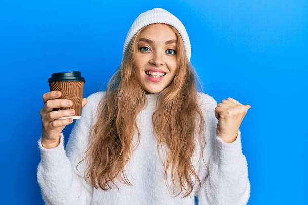 Красивая блондинка-кавказка пьет чашку кофе, указывая пальцем в сторону улыбаясь счастливой с открытым ртом  - Фото, изображение