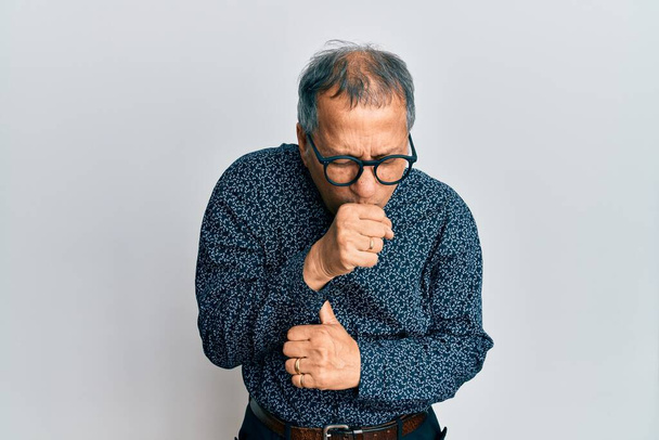 Indischer Mann mittleren Alters, der lässige Kleidung und Brille trägt, fühlt sich unwohl und hustet als Symptom für Erkältung oder Bronchitis. Gesundheitskonzept.  - Foto, Bild